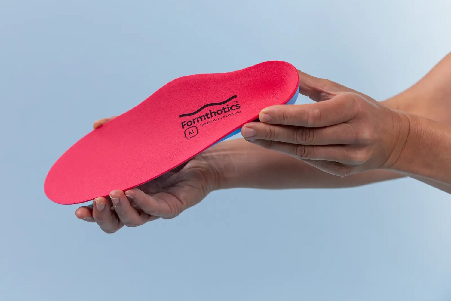 A Formthotics custom medical orthotic insole presented in two hands